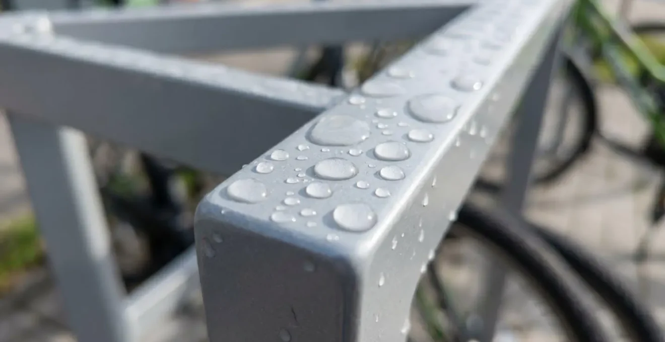 Gros plan sur des gouttes de condensation perlant sur une structure métallique d'abri vélo, texture crisp avec arrière-plan flouté